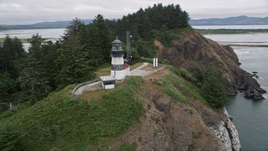 Aerial tracking shot of the Cape Disappointment Light perched atop coastal cliffs showcasing the picturesque Washington shoreline during summer
