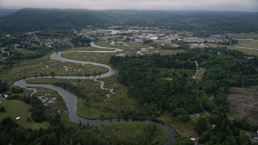 Aerial footage showcasing small town Raymond Washington located beside the scenic Willapa River with lush vegetation in an overcast day