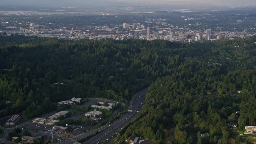 A stunning aerial view of Highway 26 as it stretches through a forest area leading to the towering high rises and downtown Portland during a beautiful sunset in the summer