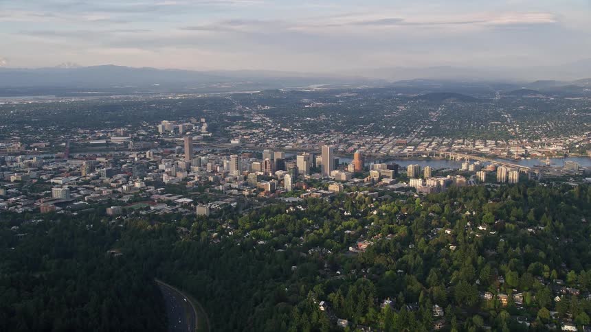 Aerial view of Downtown Portland at sunset with high-rise buildings partly cloudy skies and the Willamette River flowing through the city
