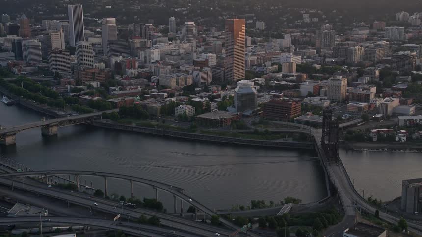  aerial footage flying by downtown Portland Oregon at sunset passing near Steel Bridge with high-rise buildings city rivers and partially cloudy skies in view