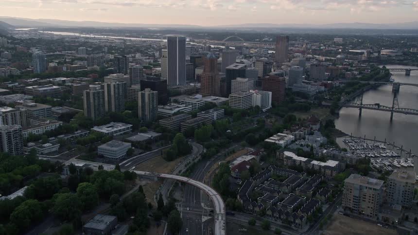 Aerial footage of downtown Portland Oregon at sunset capturing the approach and flyover of KOIN Center and Wells Fargo Center amidst a metropolis with skyscrapers and bridges