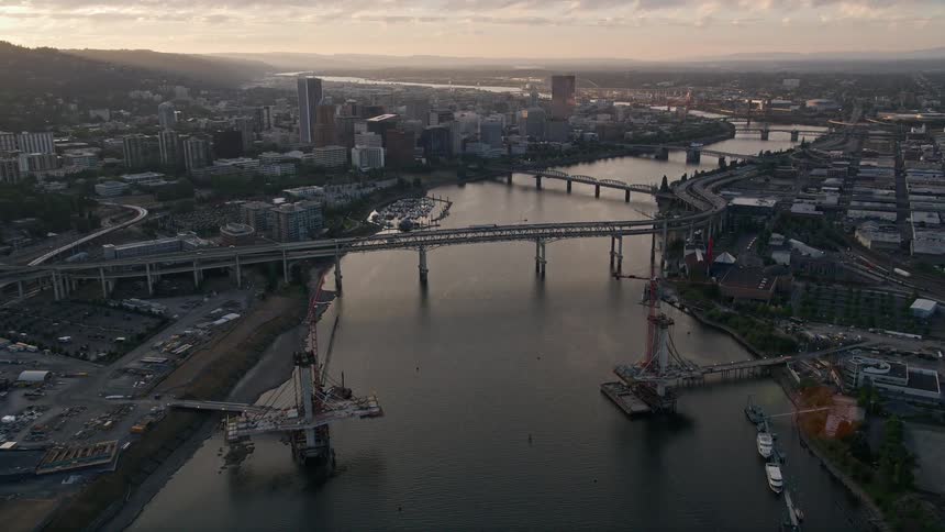 Aerial footage of bridges and Downtown Portland Oregon at dusk showcasing the city's high-rise buildings and transportation amidst a picturesque sunset over the waterways
