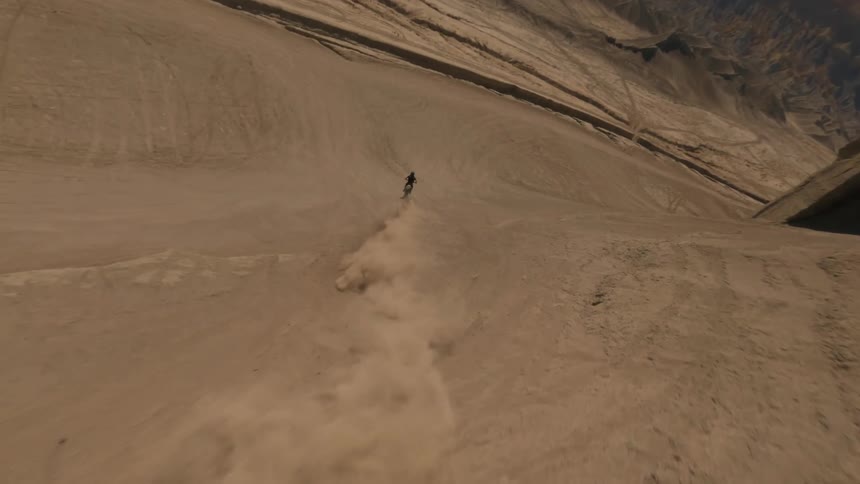A person rides up and down a sandy mountain on a motorcycle in a desert