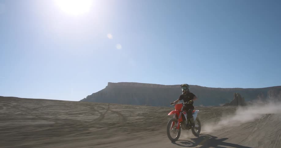 A boy riding a motorcycle across a sandy area does a wheelie