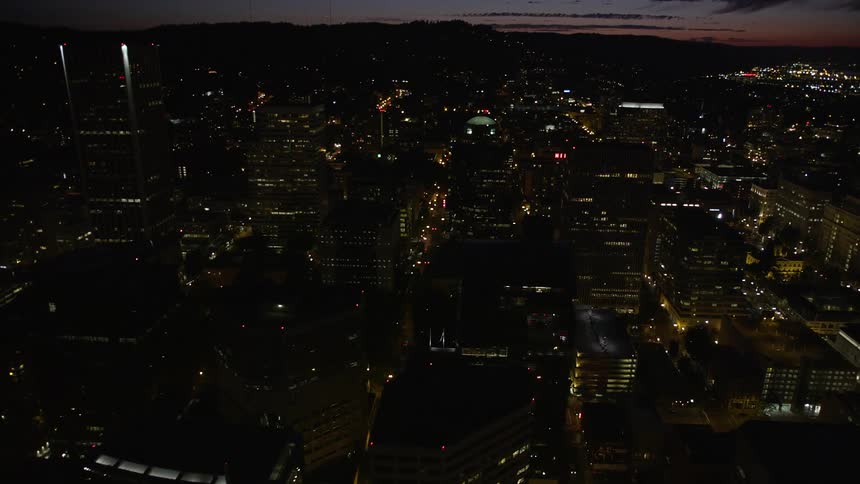  aerial footage flying over illuminated buildings in downtown Portland at night showcasing the metropolis and its high-rises during a partly cloudy evening