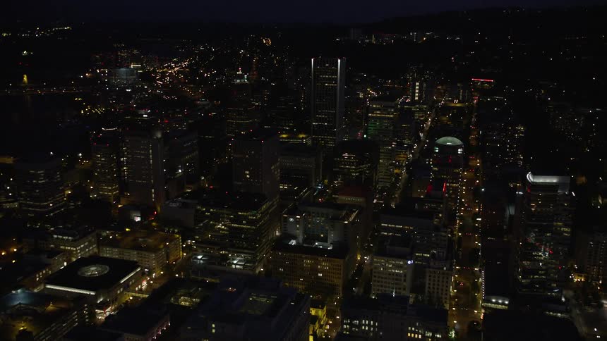 Fly over downtown Portland at night approaching the KOIN Center and Wells Fargo Center with city lights illuminating the metropolis below