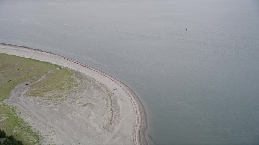 Aerial footage of a car parked on an empty beach along the Columbia River in Clatsop Spit Oregon offering a scenic view of the shoreline and ocean water during the daytime