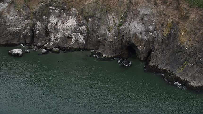 Aerial footage of a sea cave at the base of a cliff in Cape Disappointment Washington with stunning views of the coastline and the Pacific Northwest during summer
