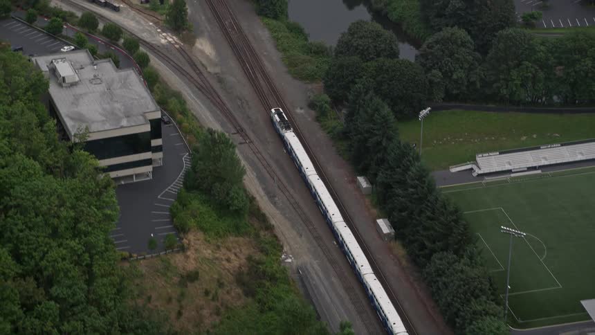 Aerial view of a commuter train tracking beneath a freeway through a lush vegetation-rich city in Tukwila Washington during summer