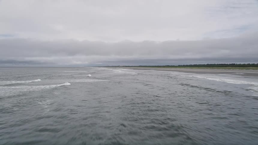 Low flying aerial footage captures the beauty of crashing waves and an empty beach on the coast of Ilwaco Washington offering a scenic and serene view of the Pacific Northwest during the summer