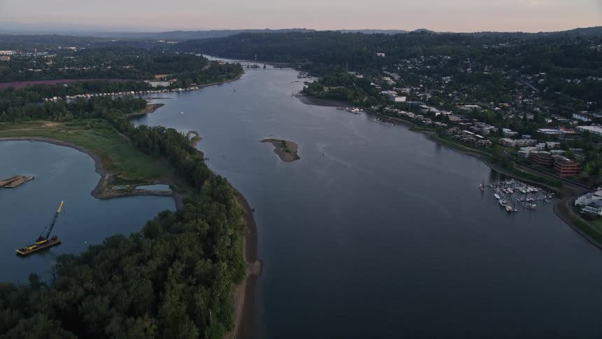 Aerial view at sunset of Willamette River approaching Toe Island and Ross Island in Portland Oregon with partly cloudy skies and the city skyline in the background
