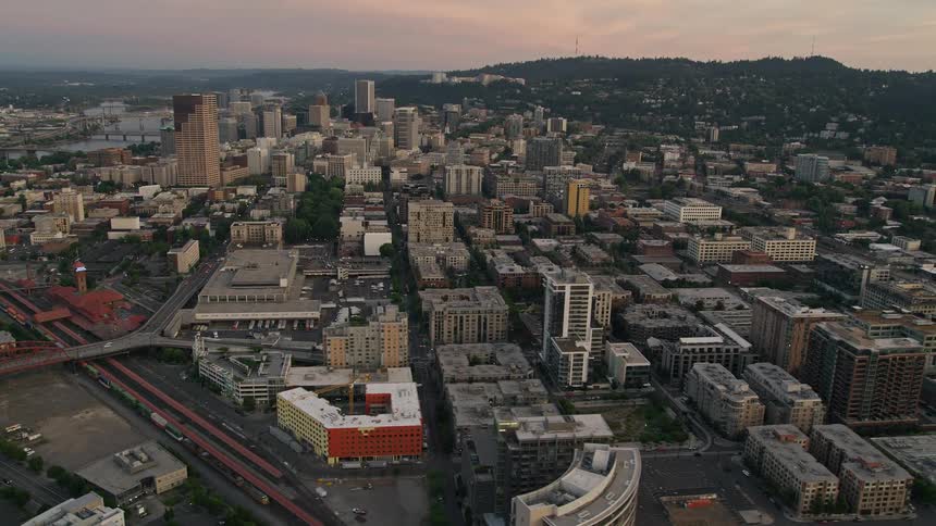 an aerial view of Downtown Portland Oregon at twilight showcasing the city's high-rise buildings bustling metropolitan atmosphere and partly cloudy skies