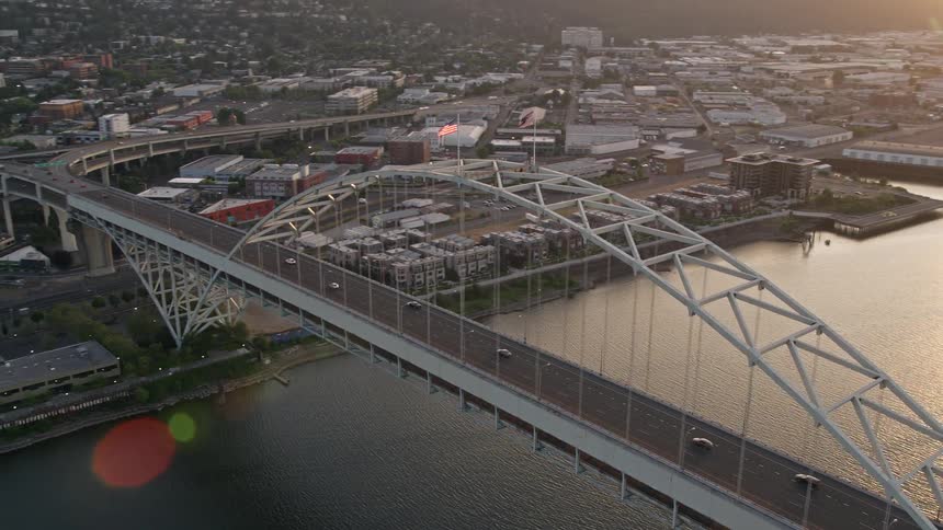 Aerial footage of cars driving over the arched Fremont Bridge in Portland Oregon revealing the bustling downtown area at sunset