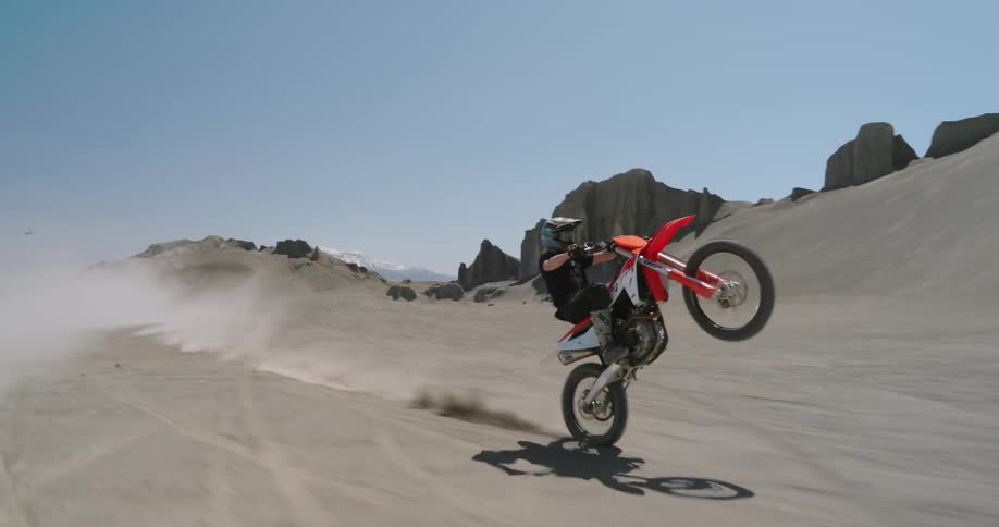 Person with helmet rides dirt bike lifting front wheel in the desert