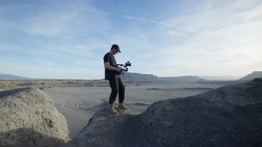 A man on top of a rock filming with his professional camera