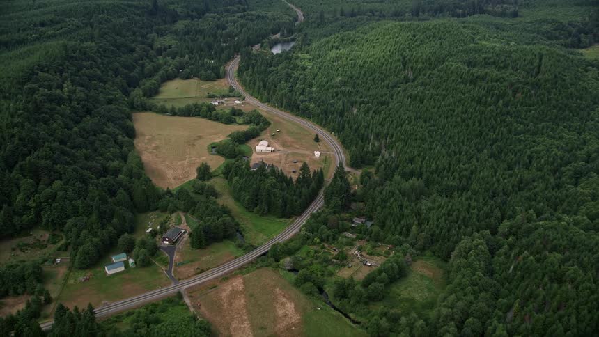 Aerial footage of a country road cutting through farmland and evergreen forest in Mason County Washington during summer