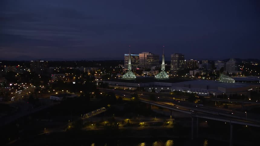 Aerial twilight view of lit spires atop the Oregon Convention Center in the Lloyd District of Northeast Portland with office buildings transportation and the Steel Bridge in the background