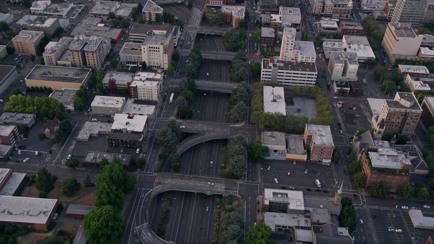 Sunset aerial footage showcases bird's eye view of downtown Portland Oregon with light traffic on Interstate 405 during a partly cloudy evening