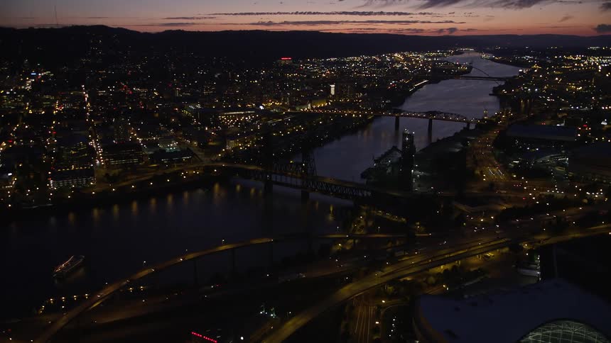  aerial footage capturing the picturesque metropolis of downtown Portland Oregon with its high-rise towers iconic bridges along the Willamette River and the warm twilight glow of a summer evening