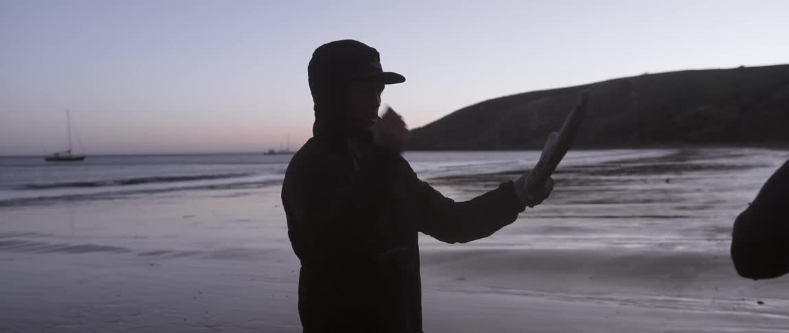 A man is walking along the beach with a branch