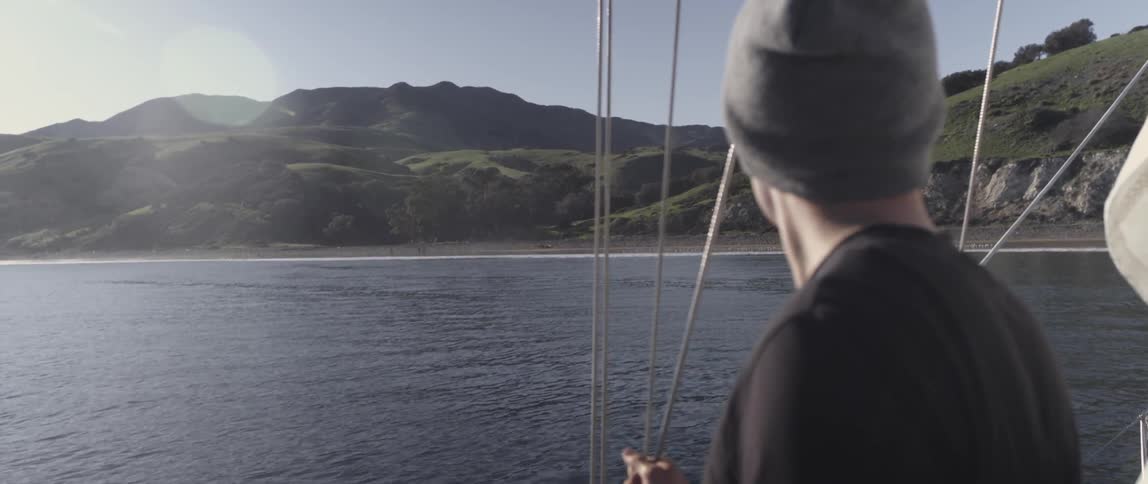 A man is holding onto the ropes of a boat as it sails