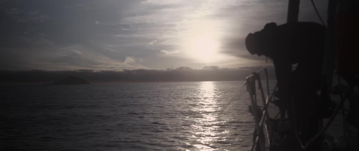 A man leans over the side of a boat at sunset