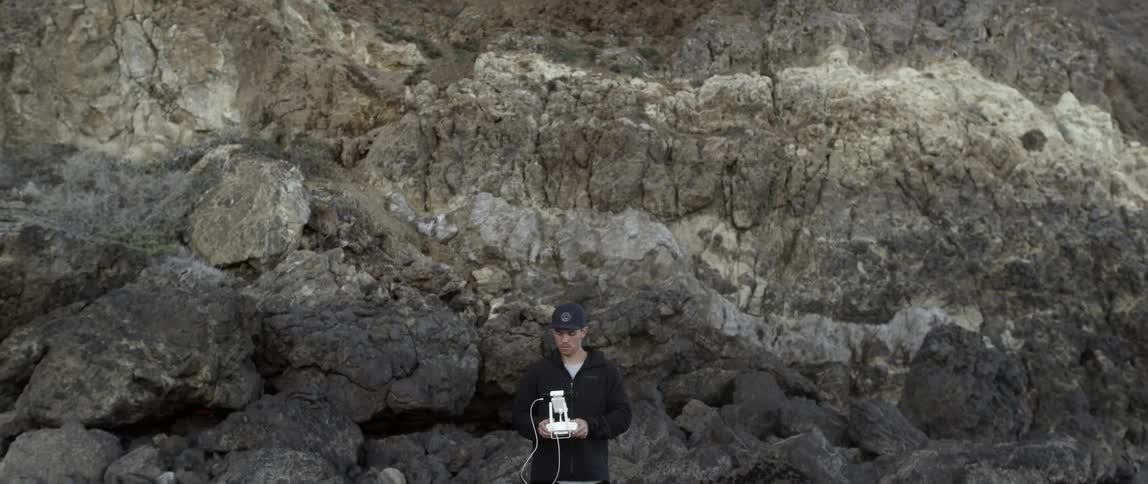 A man is standing in front of rocks using a drone controller