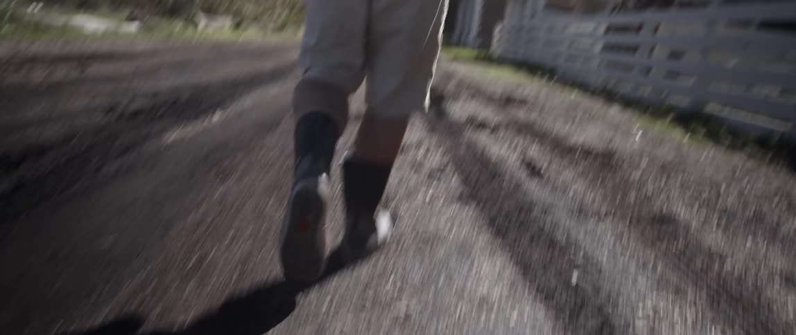 A man walks on a dirt trail by a farm