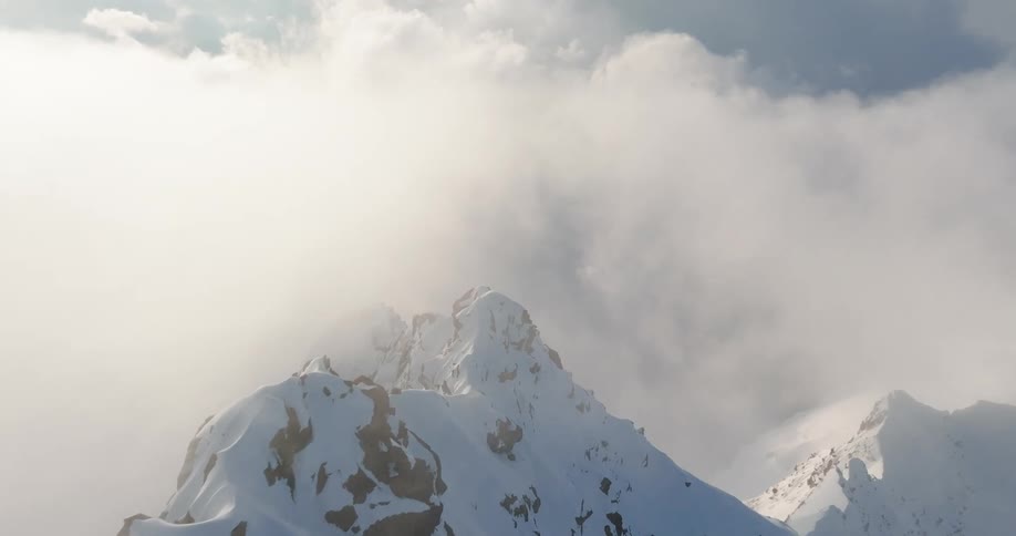 Snow completely covers a rocky mountain range that is engulfed in a layer of clouds