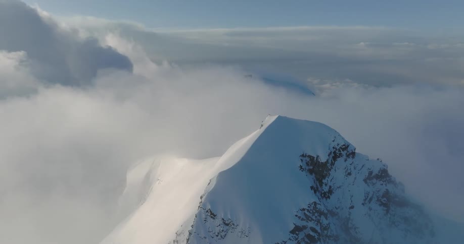 Aerial view of a mountain at cloud level covered in snow