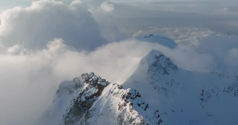 An aerial view of mountains with icy snowy peaks and big clouds