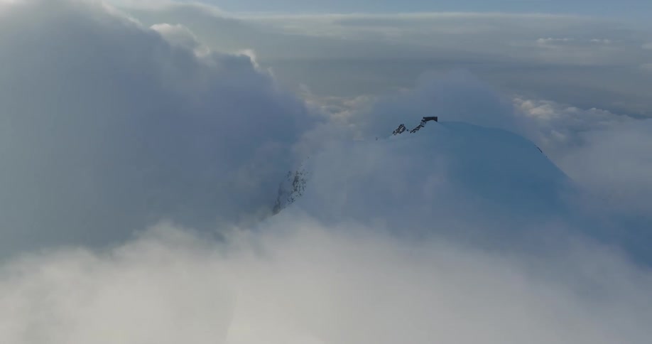 Snow covered mountain summit breaks through clouds