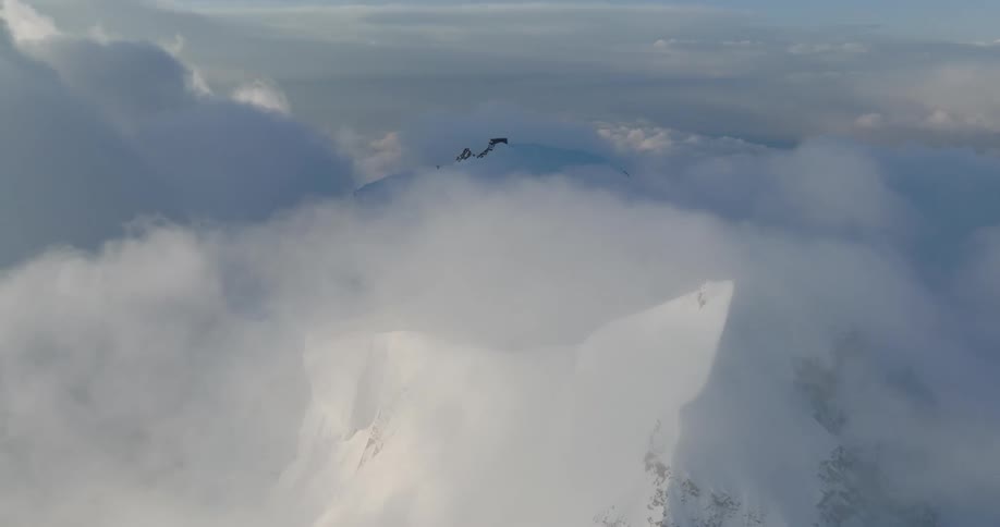 An enormous mountain range is covered in snow and enveloped in clouds