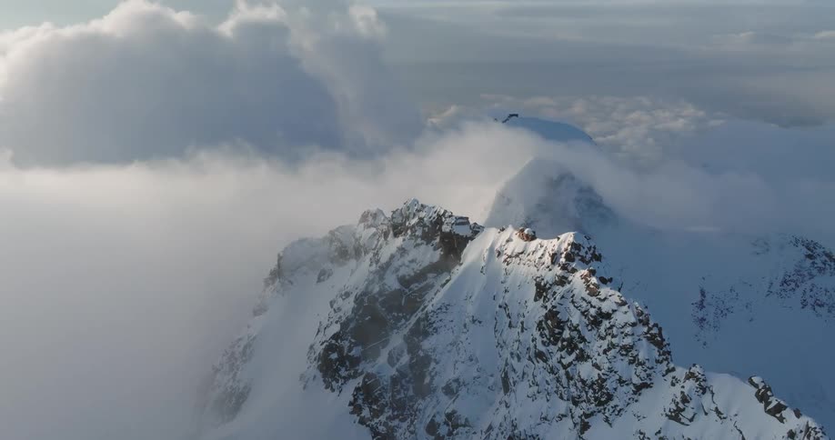 An aerial view of a mountain peak with snow and big clouds in the sky