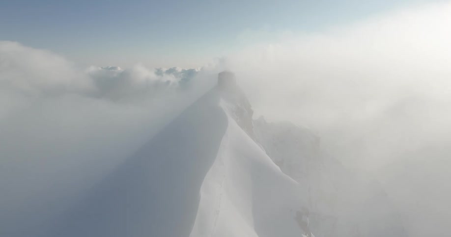 Aerial of a mountain peak covered in snow under the clouds