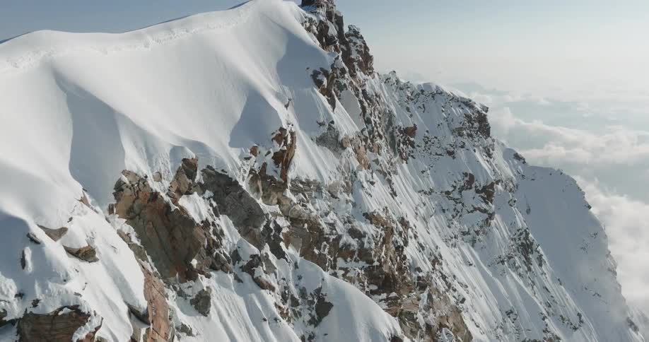 Aerial of a rocky mountain covered with snow and a house on top