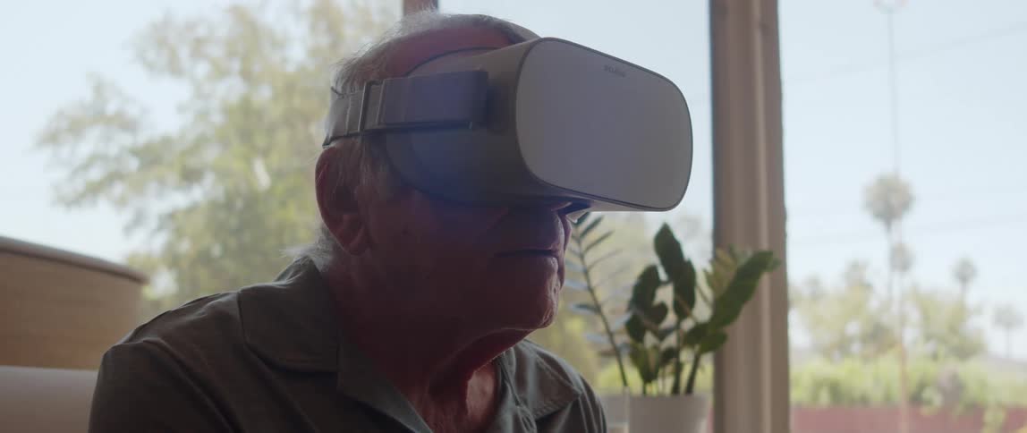 An elderly man wearing a virtual reality headset looks around within the virtual environment