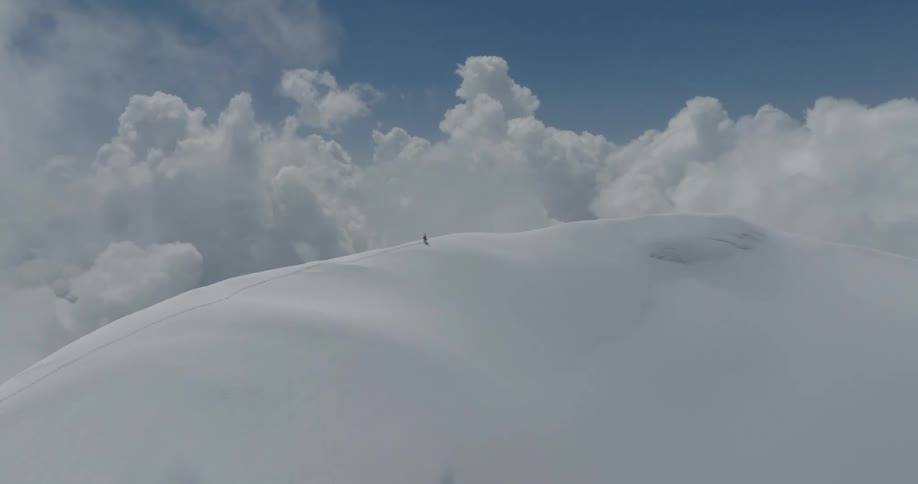 Mountains at cloud level covered in snow with a person hiking