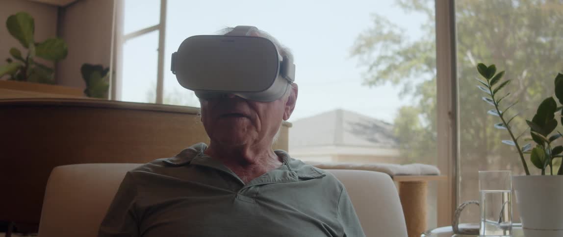 Elderly man sitting on a chair with a virtual reality headset attached to his face