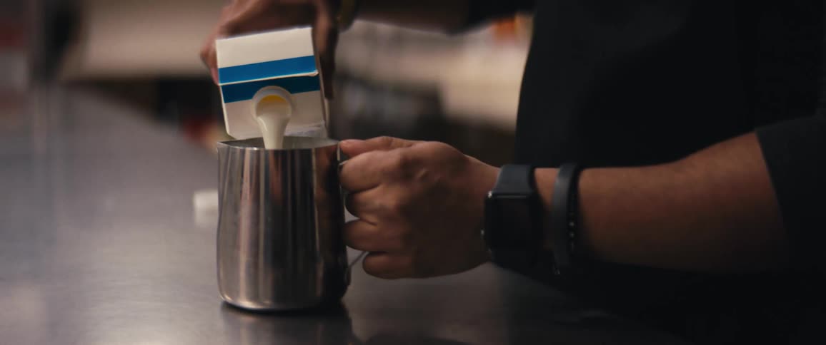A man pouring carton milk into a metal mug