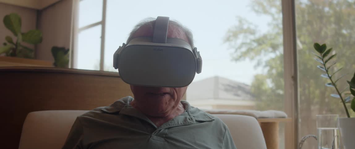 An elderly man wearing a virtual reality headset while sitting indoors