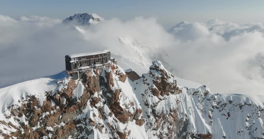 Lodge sits on snow covered mountain ridge among clouds