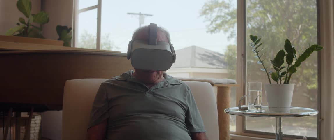 An elderly man sitting with a virtual reality headset on his head