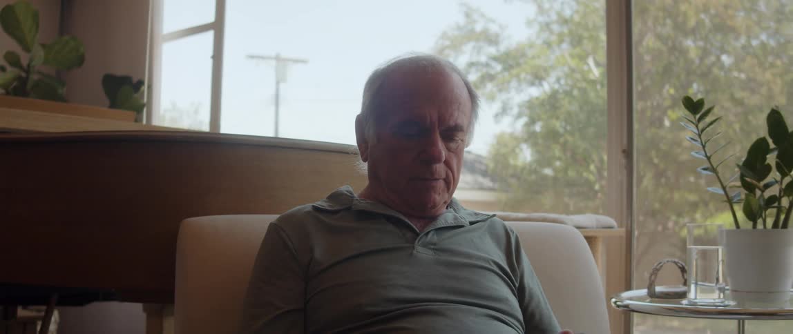 An old man sitting down fiddling with a cell phone in his hands