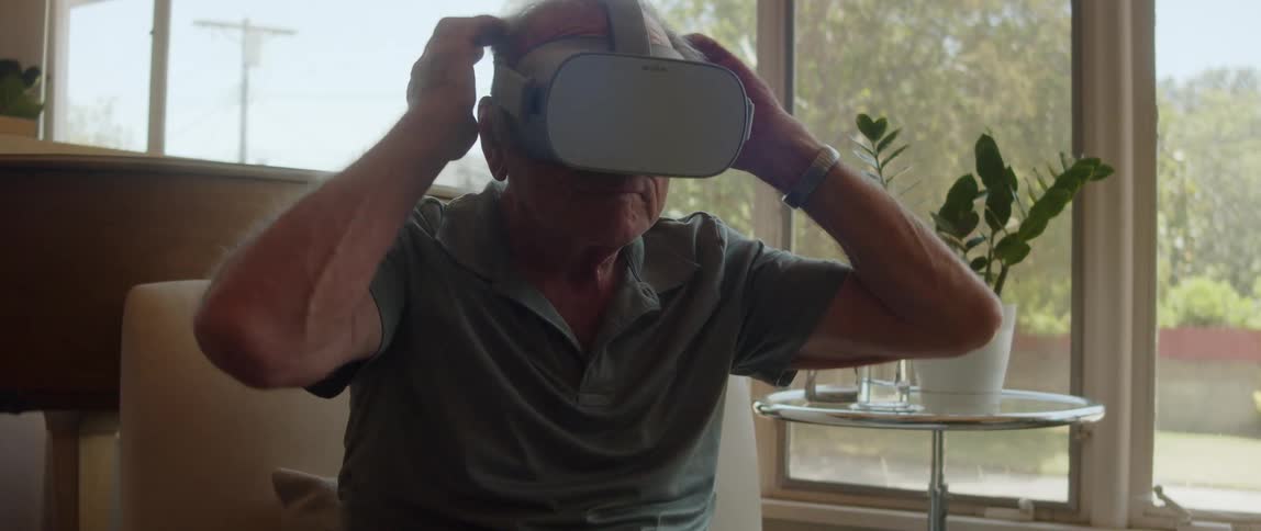 A man is sitting down and putting on virtual reality headset