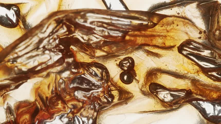 Amber colored iced beverage forms bubbles in glass