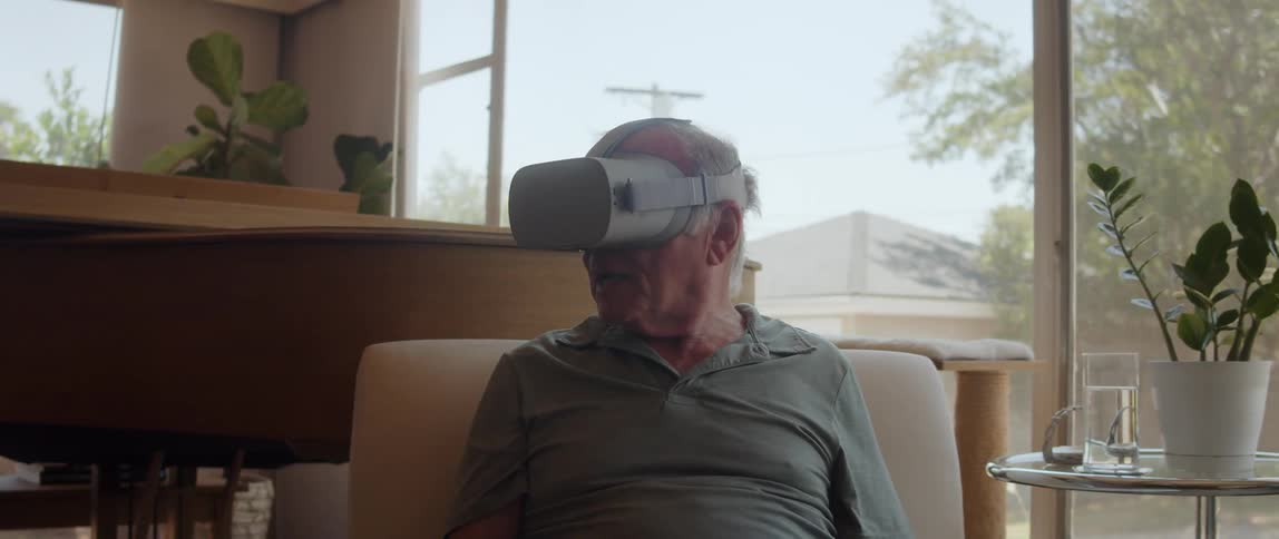 An elderly man sitting and with virtual reality glasses looking to the sides