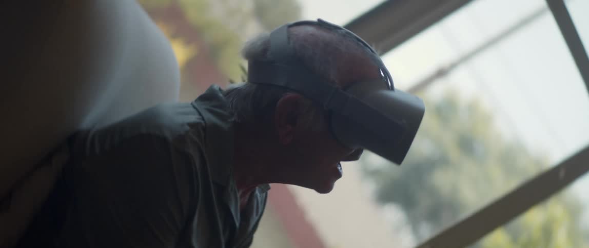 Old man with a virtual reality headset sitting on a chair indoors during the day