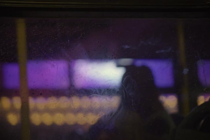 A window of a vehicle with drops of water and behind is passing some advertisements on screens